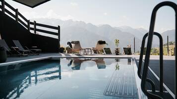 A pool area with lounge chairs and a view of mountains.