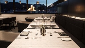 A restaurant with a long table set for dining, a sofa, and a view of the mountains through large windows.