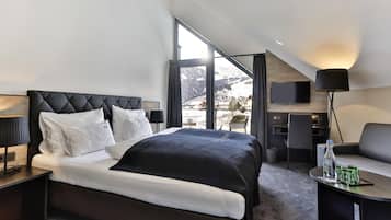 A modern hotel room with a large bed, a desk, a chair, a TV, and a view of a snowy landscape.
