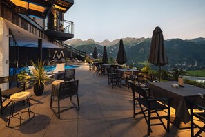 An outdoor patio with tables and chairs, a pool, and mountain views.