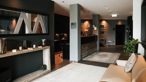 A modern hotel lobby with a reception desk, a large abstract artwork, and a seating area with a sofa and a coffee table.