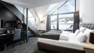 A modern hotel room with a large bed, a desk, and a view of a snowy landscape through large windows.