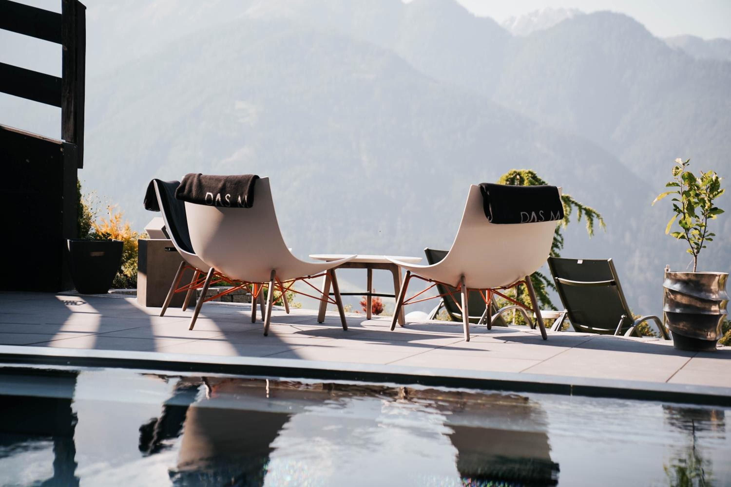 Ein Poolbereich mit zwei Stühlen, einem Tisch, einer Topfpflanze und Blick auf die Berge.