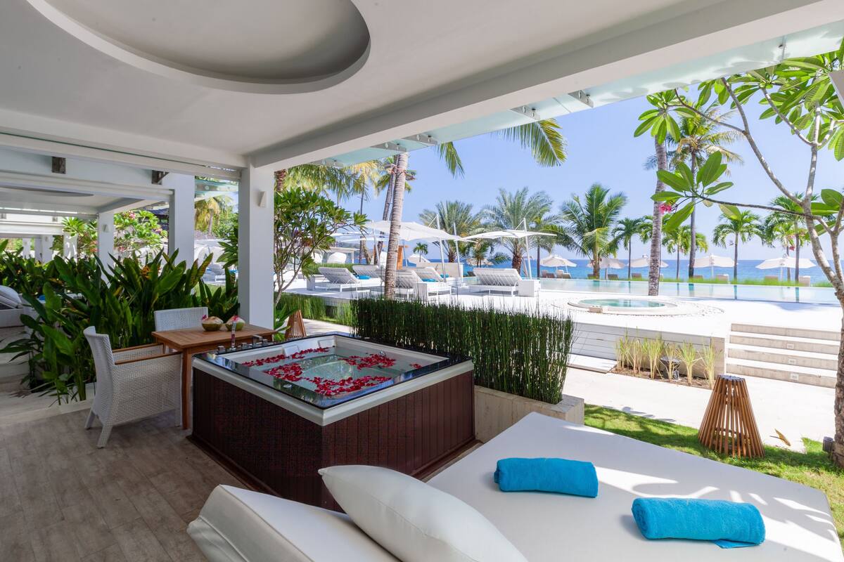 A modern outdoor lounge area with a hot tub, lounge chairs, and a view of the ocean.