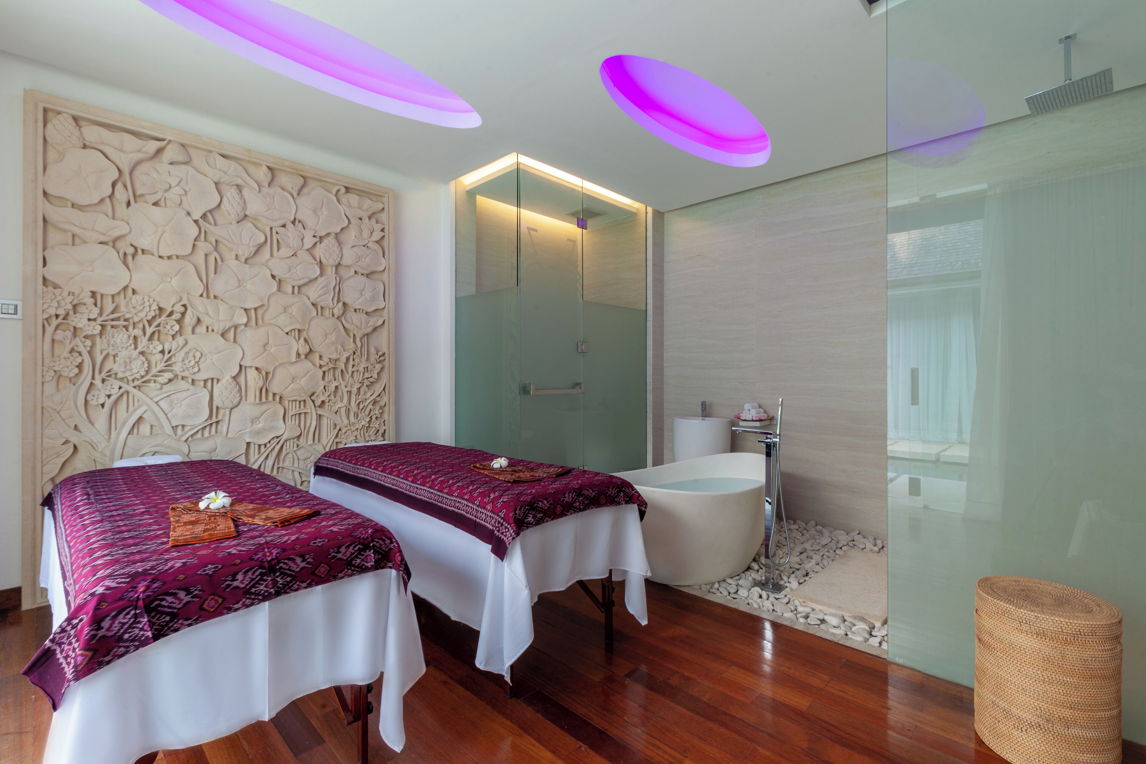 A modern spa room with two beds, a glass-enclosed shower, and a wooden floor.