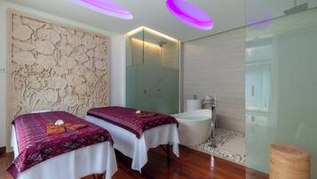 A modern spa room with two beds, a glass-enclosed shower, and a wooden floor.