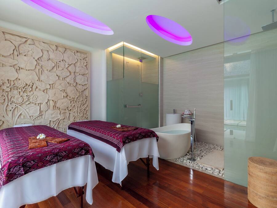 A modern spa room with two beds, a glass-enclosed shower, and a wooden floor.