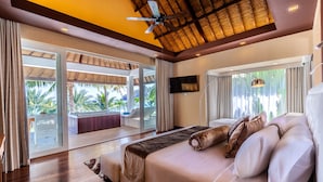 A spacious bedroom with a large bed, a ceiling fan, and a view of a pool and palm trees.