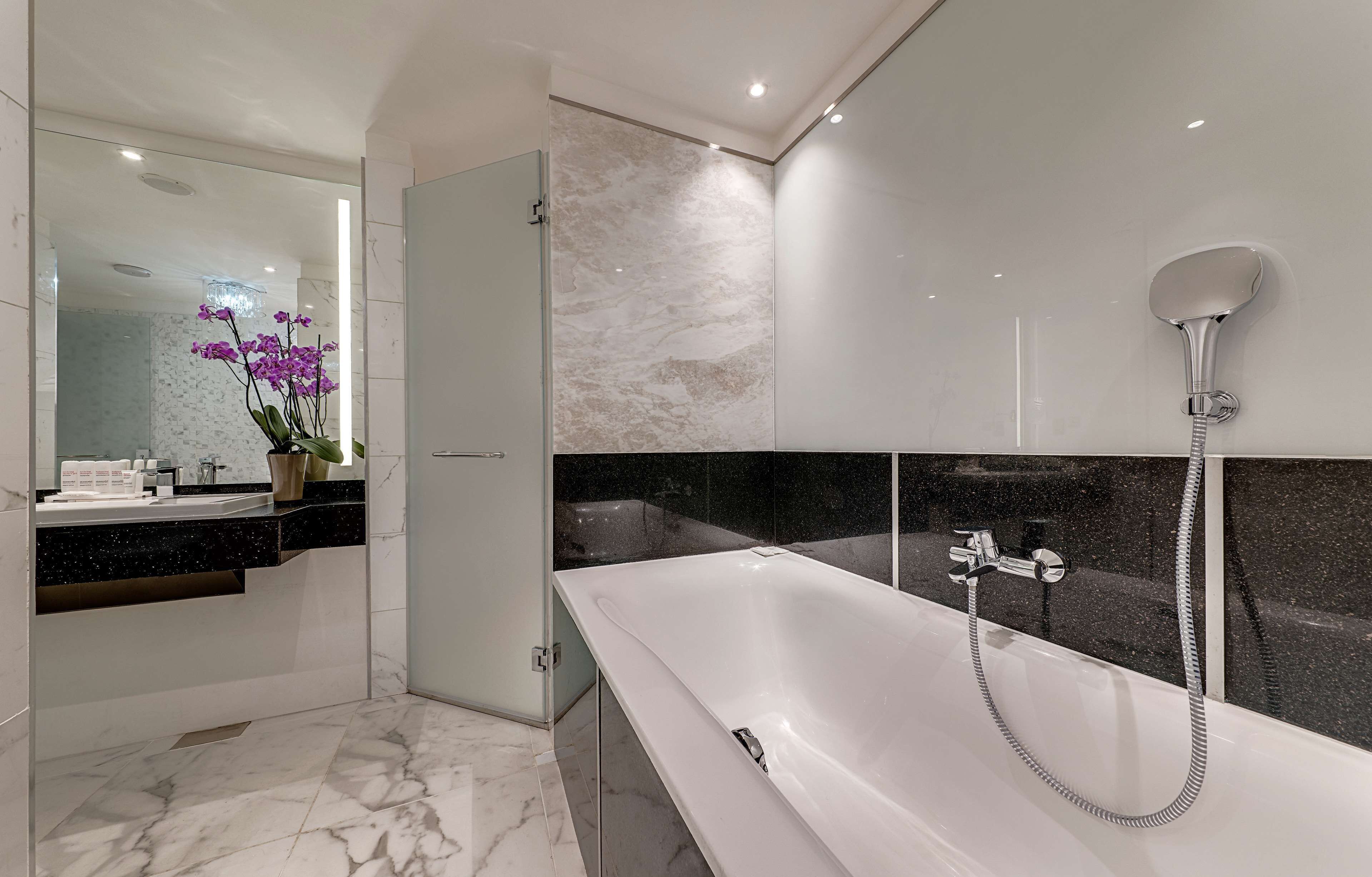 A modern bathroom with a large bathtub, a glass shower enclosure, and a marble-tiled floor.