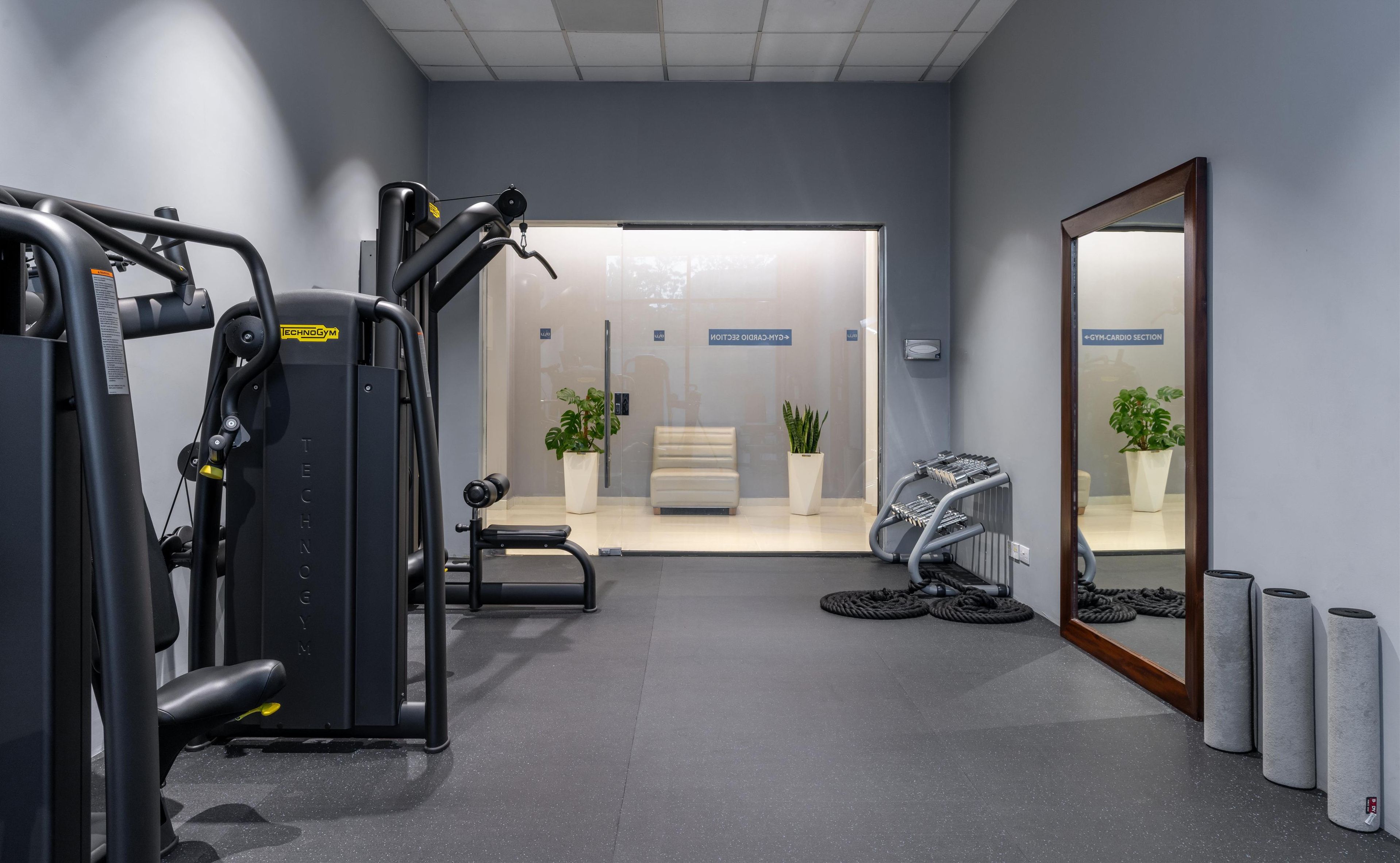A gym with cardio and strength equipment, a mirror, and a bench.
