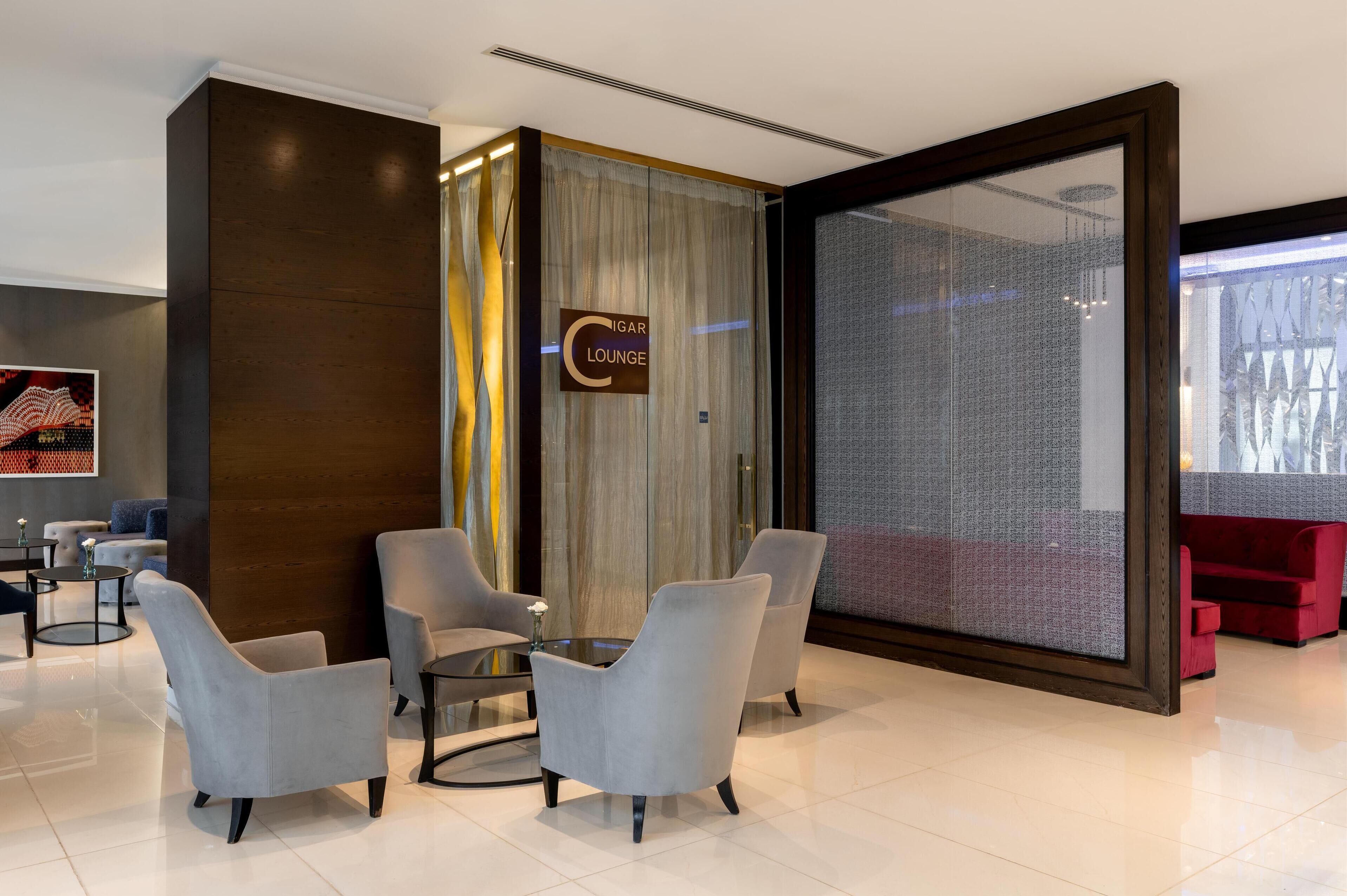 A modern lounge area with grey armchairs, a glass table, and a sign reading "Cigar Lounge".