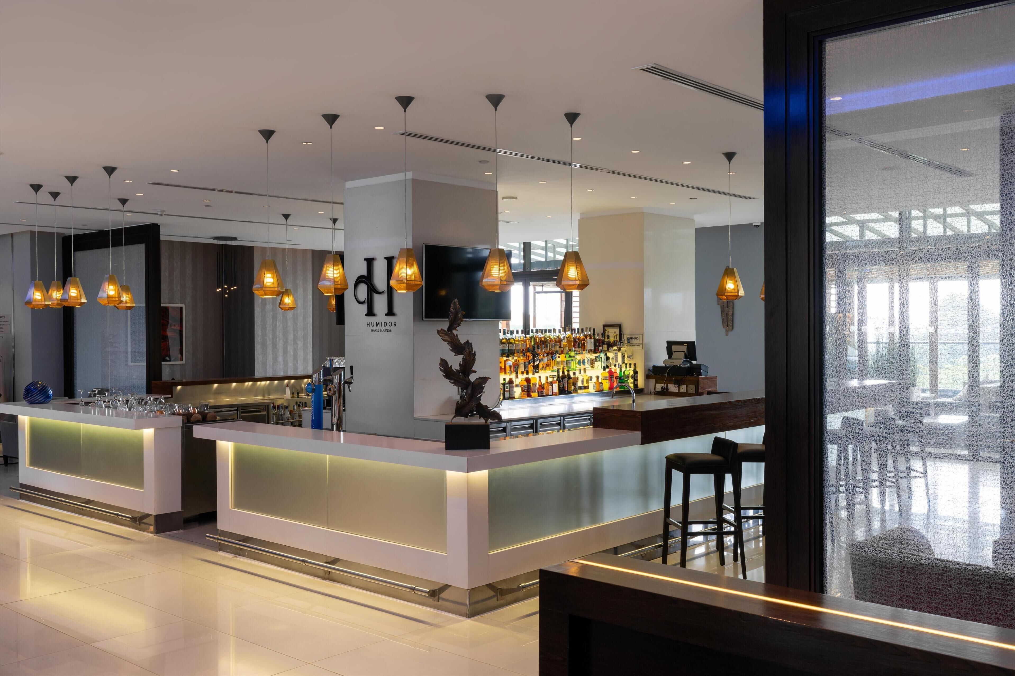 Un área de bar moderna con iluminación colgante, una gran pantalla de televisión y una barra repleta de botellas.