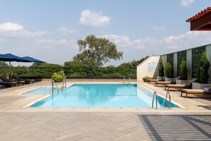 Una piscina con tumbonas y sombrillas, rodeada de vegetación y un cielo despejado.