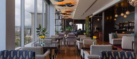 A modern hotel lobby with a long table, chairs, and a seating area with sofas.