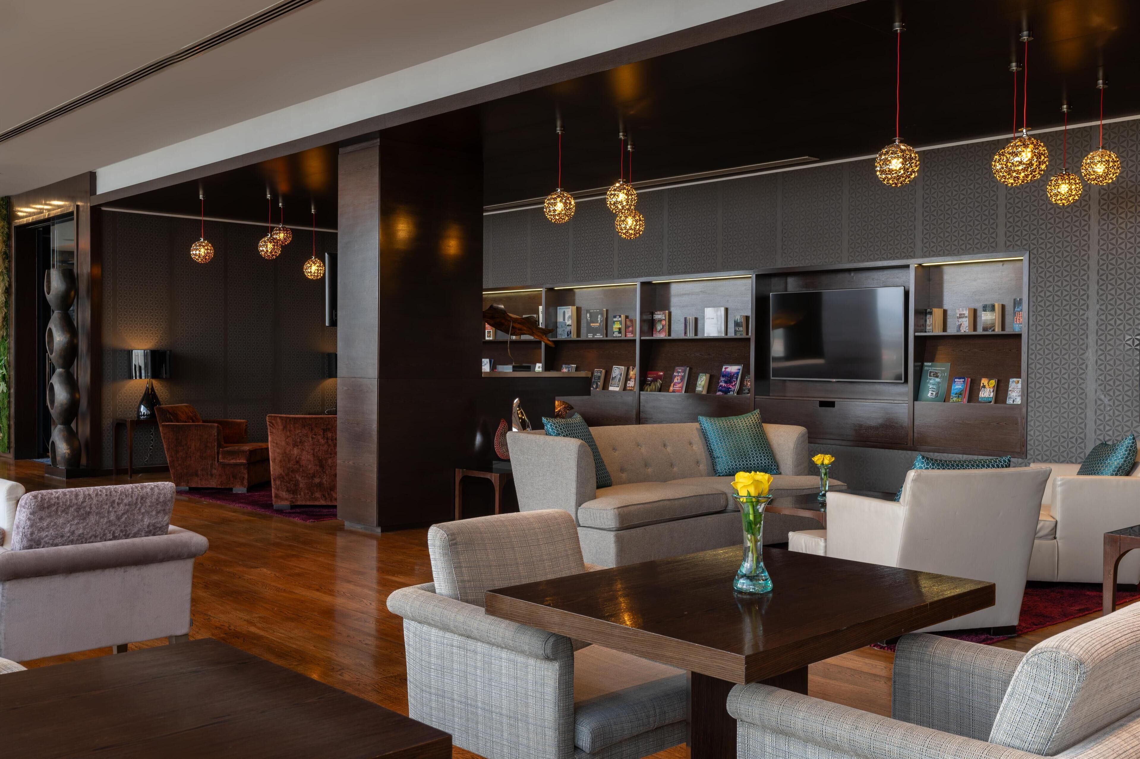 A modern living room with a large flat-screen TV, grey upholstered sofas, a coffee table, and decorative lighting.