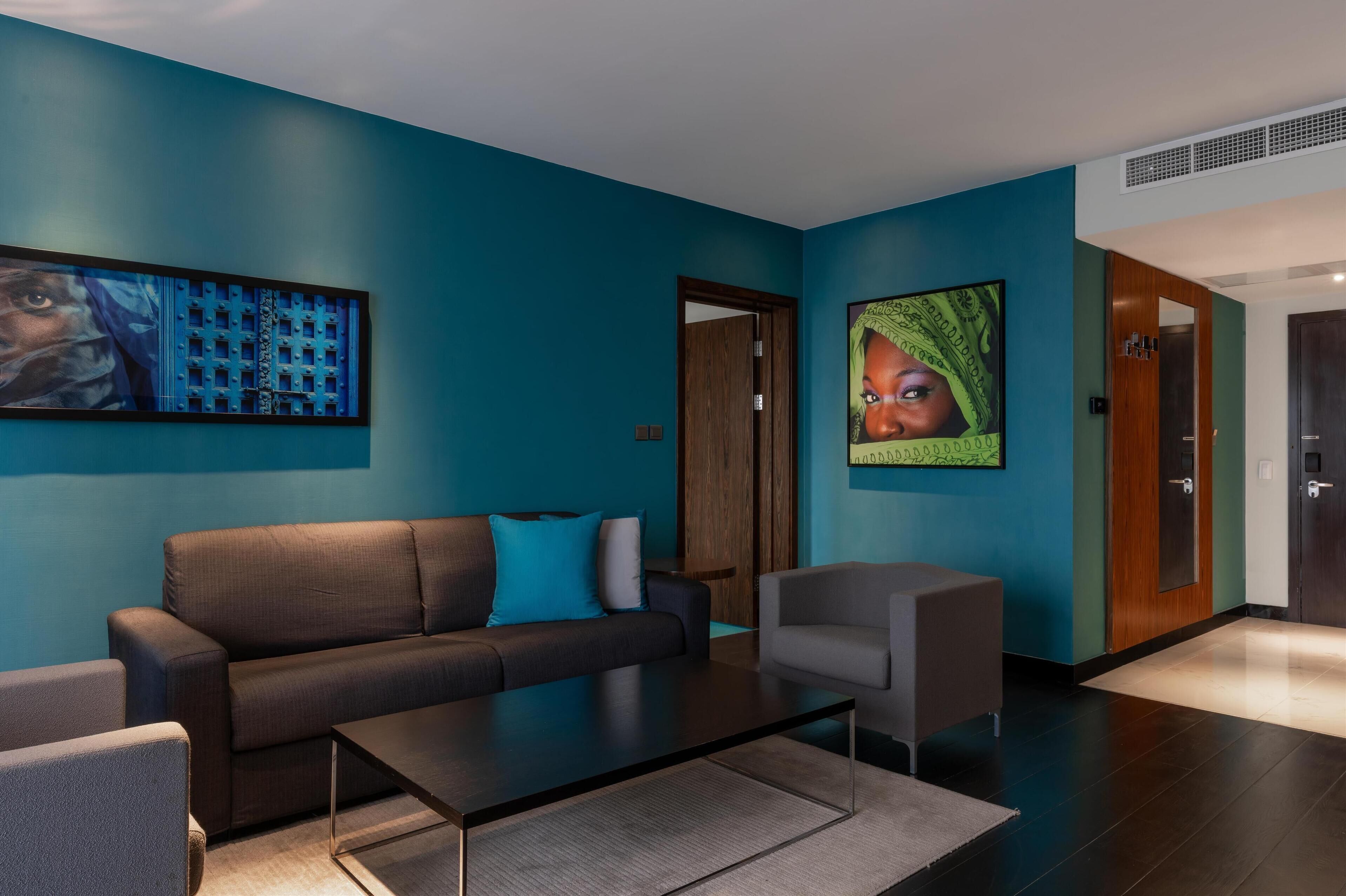 A modern hotel lobby with a teal wall, a black sofa, a gray armchair, and a coffee table.