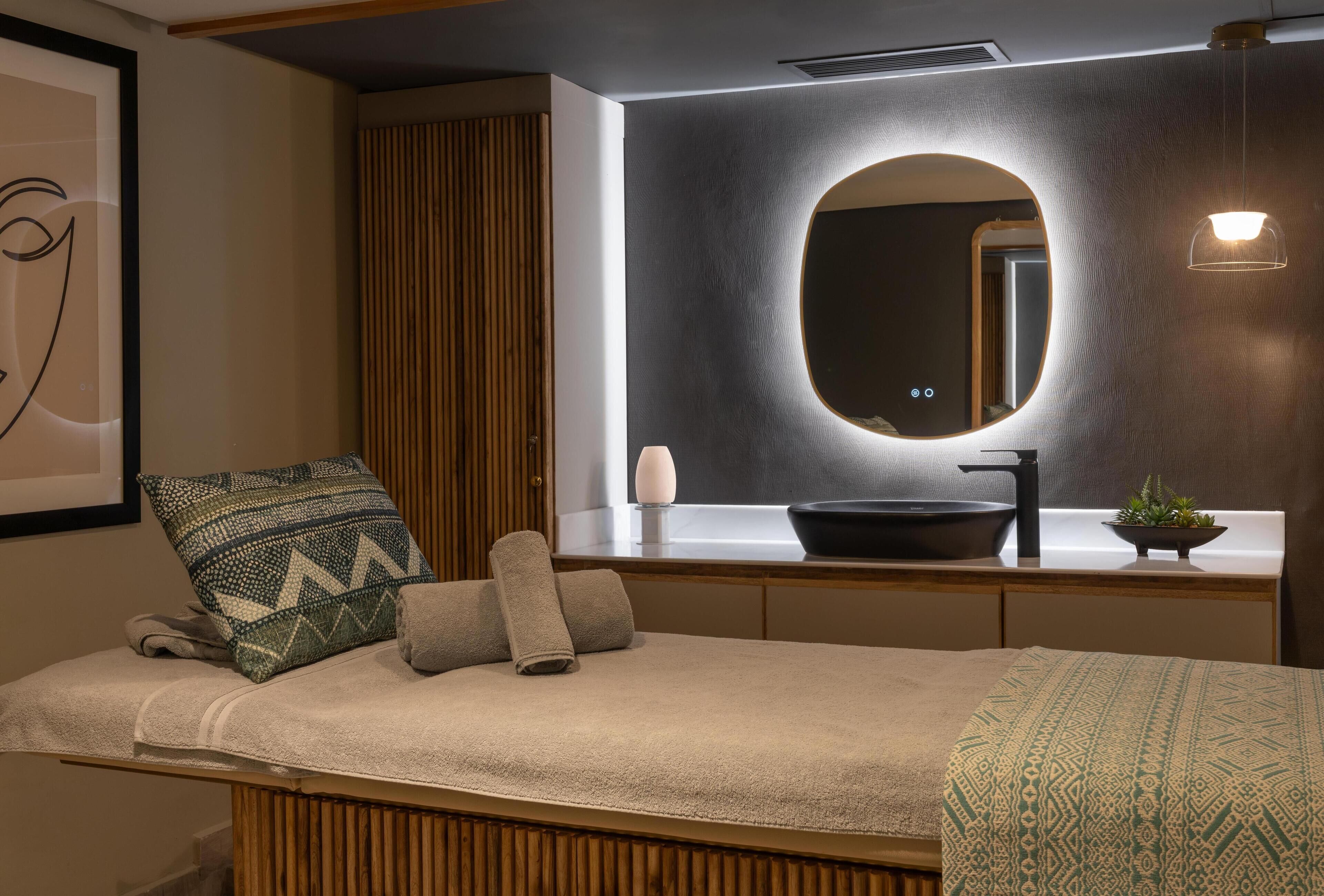 A modern bedroom with a bed, a bedside table, a mirror, and a wall-mounted light fixture.