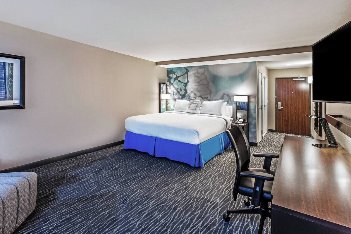 Una habitación de hotel con cama, escritorio, silla, televisor y puerta.
