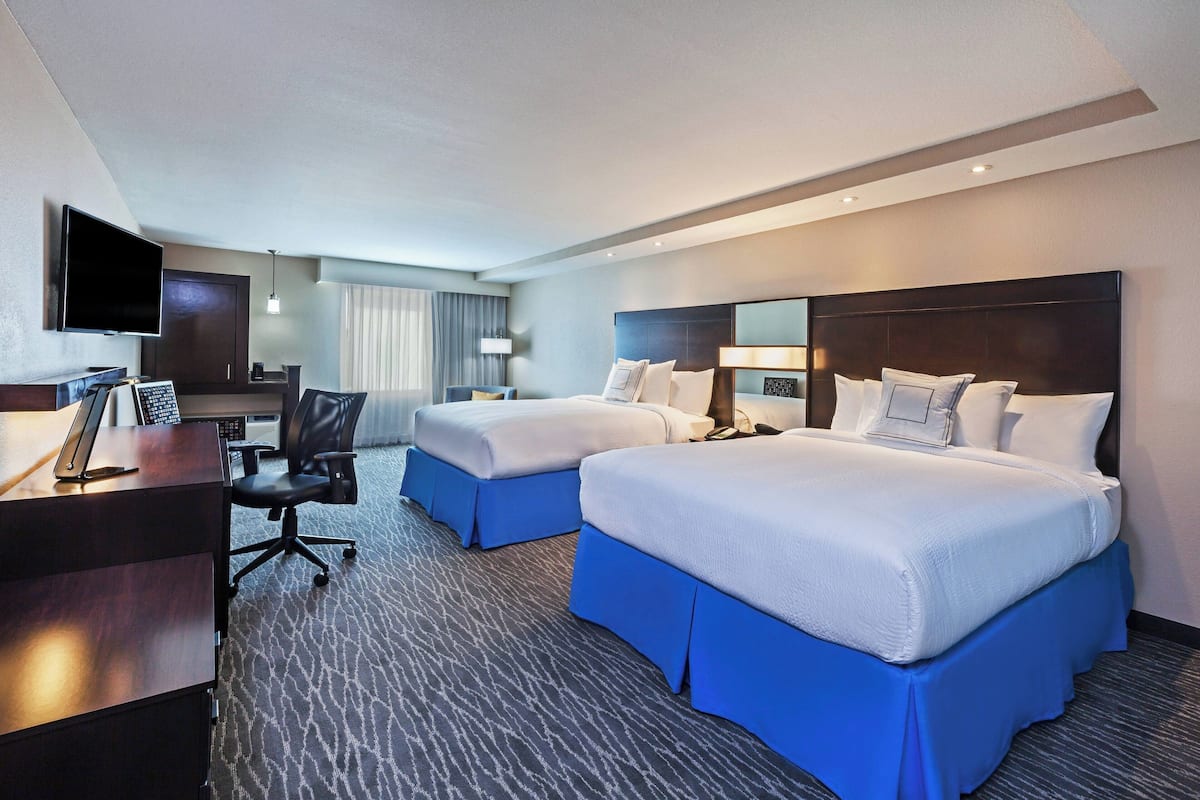 Habitación de hotel con dos camas, un escritorio con computadora, un televisor y una ventana con cortinas.