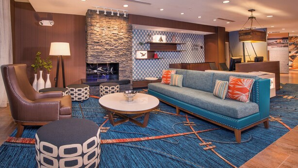 A modern lobby with a stone fireplace, a blue patterned rug, a blue sofa with colorful cushions, a brown leather chair, and a round coffee table.