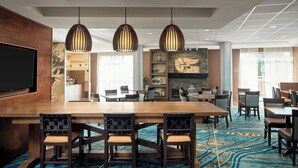 A hotel lobby with a large wooden reception desk, multiple seating areas, a television, and a patterned carpet.