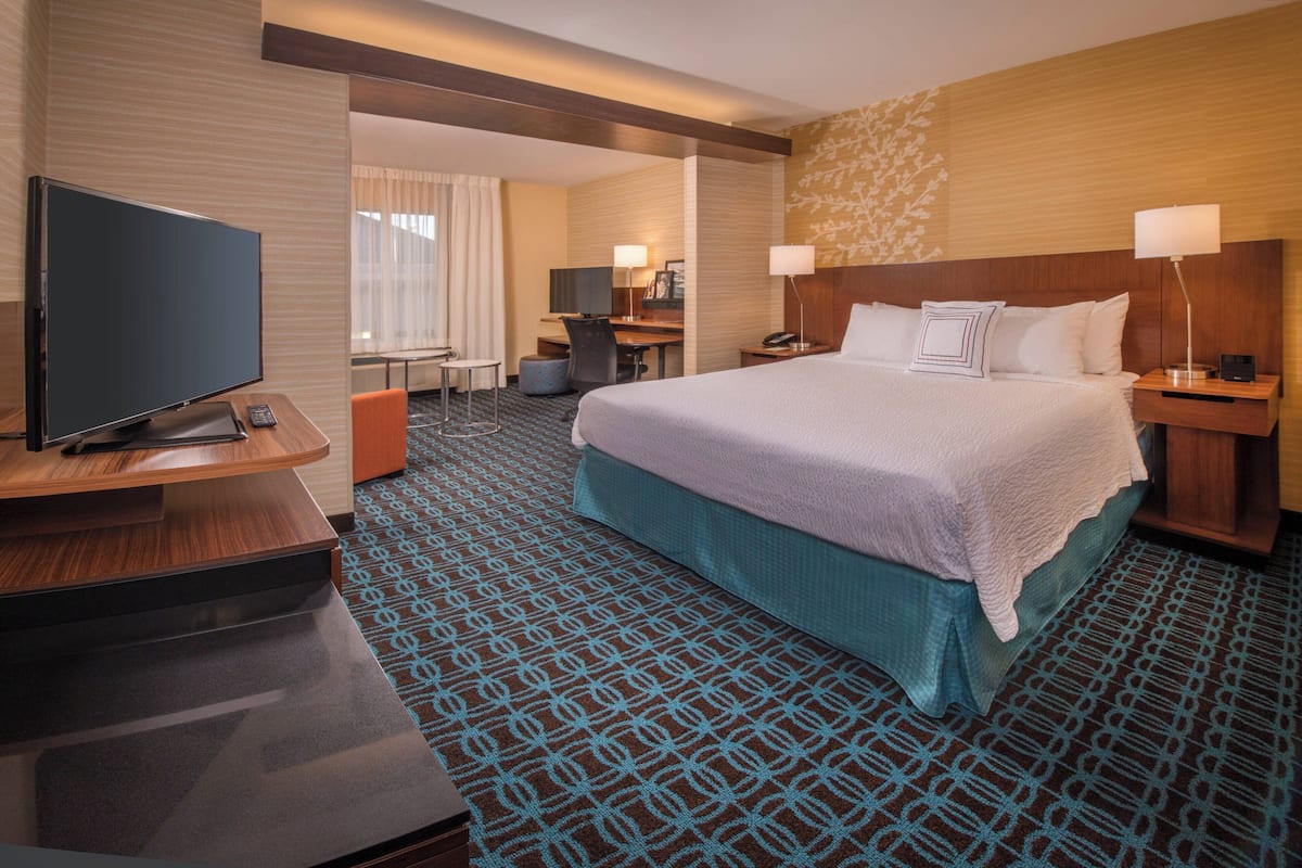 Ein Hotelzimmer mit einem großen Bett, einem Schreibtisch, einem Fernseher und einer Schreibtischlampe.