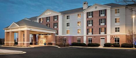 A multi-story hotel with a covered entrance, a brick facade, and a parking lot.