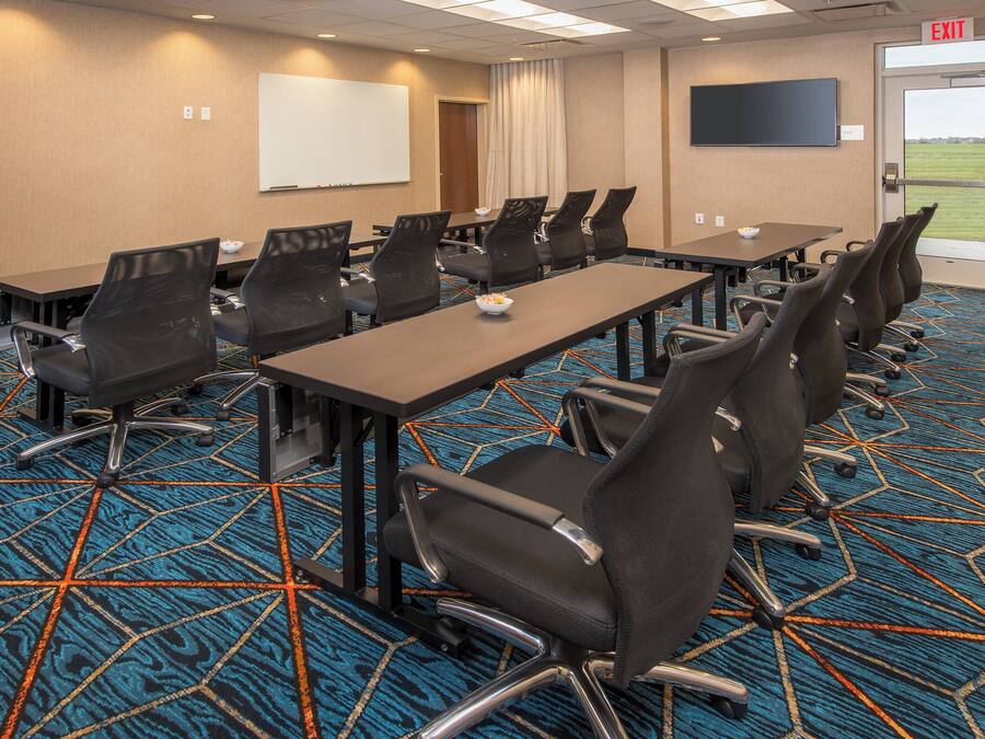 A conference room with multiple tables and chairs, a whiteboard, and a television screen.