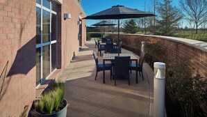 An outdoor patio with tables and chairs, a large umbrella, and a brick building in the background.