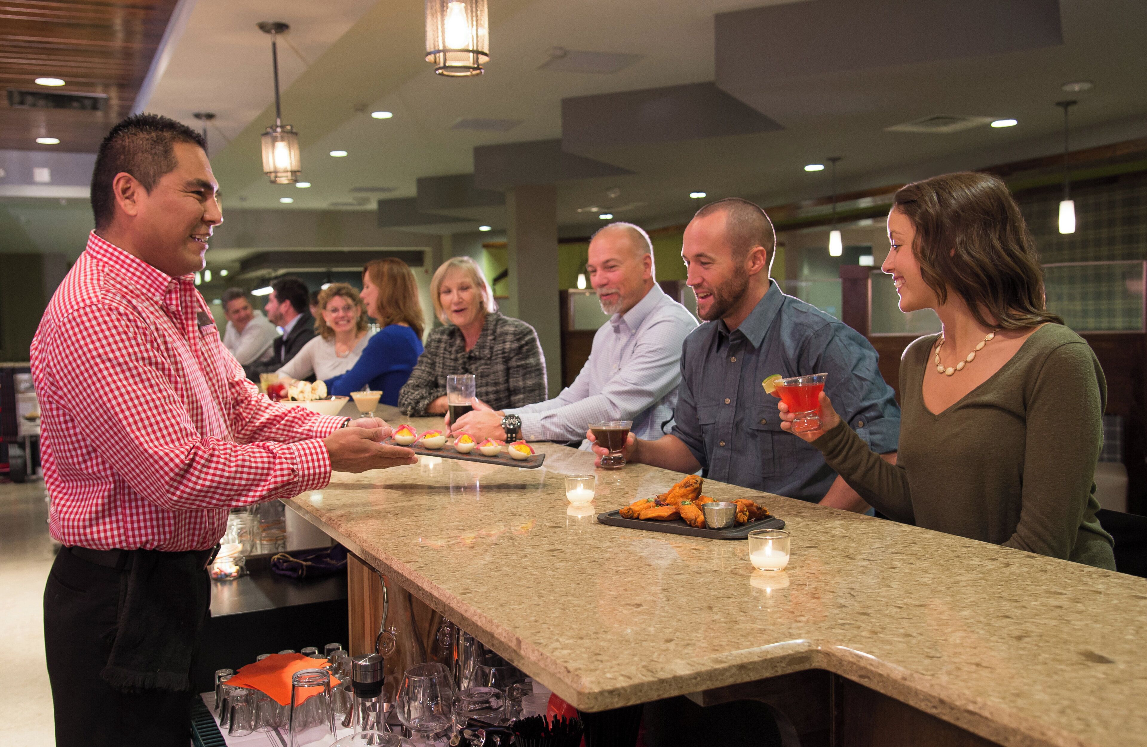 A bar area with a counter, glasses, and a tray of food.