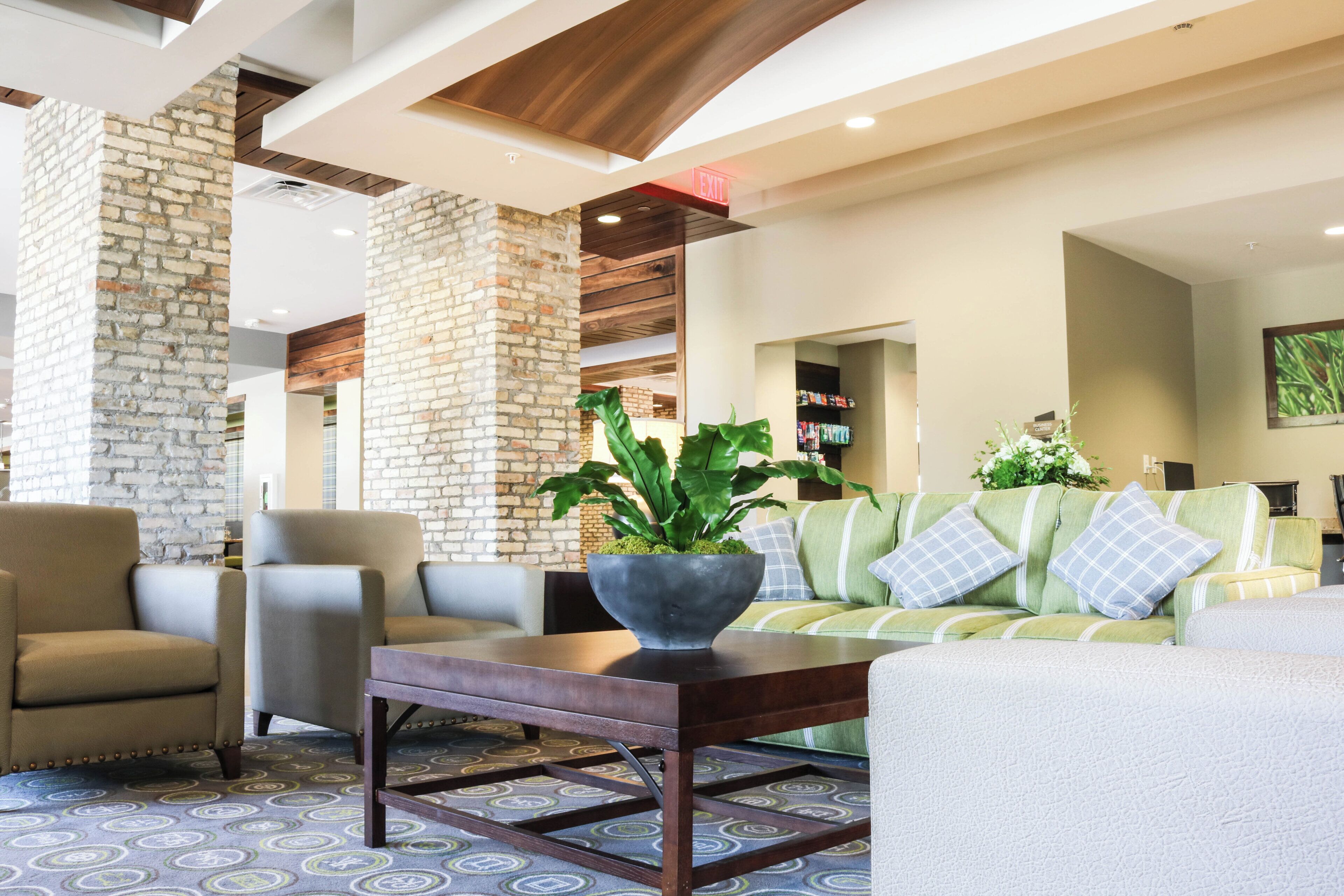 A lobby with a brick wall, a sofa with patterned cushions, and a coffee table with a plant.