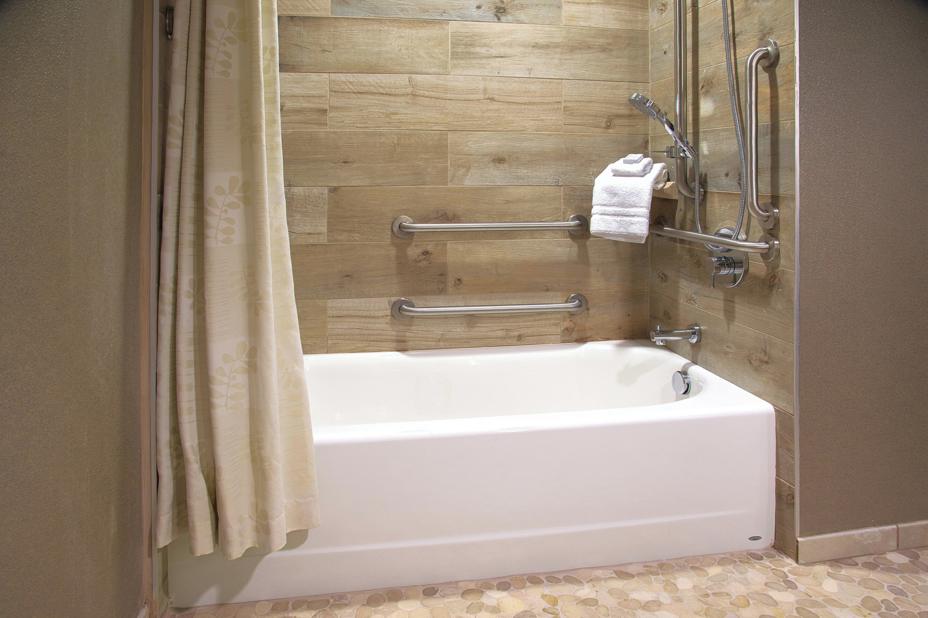 A bathtub with a wooden wall backdrop, a grab bar, and a towel rack.