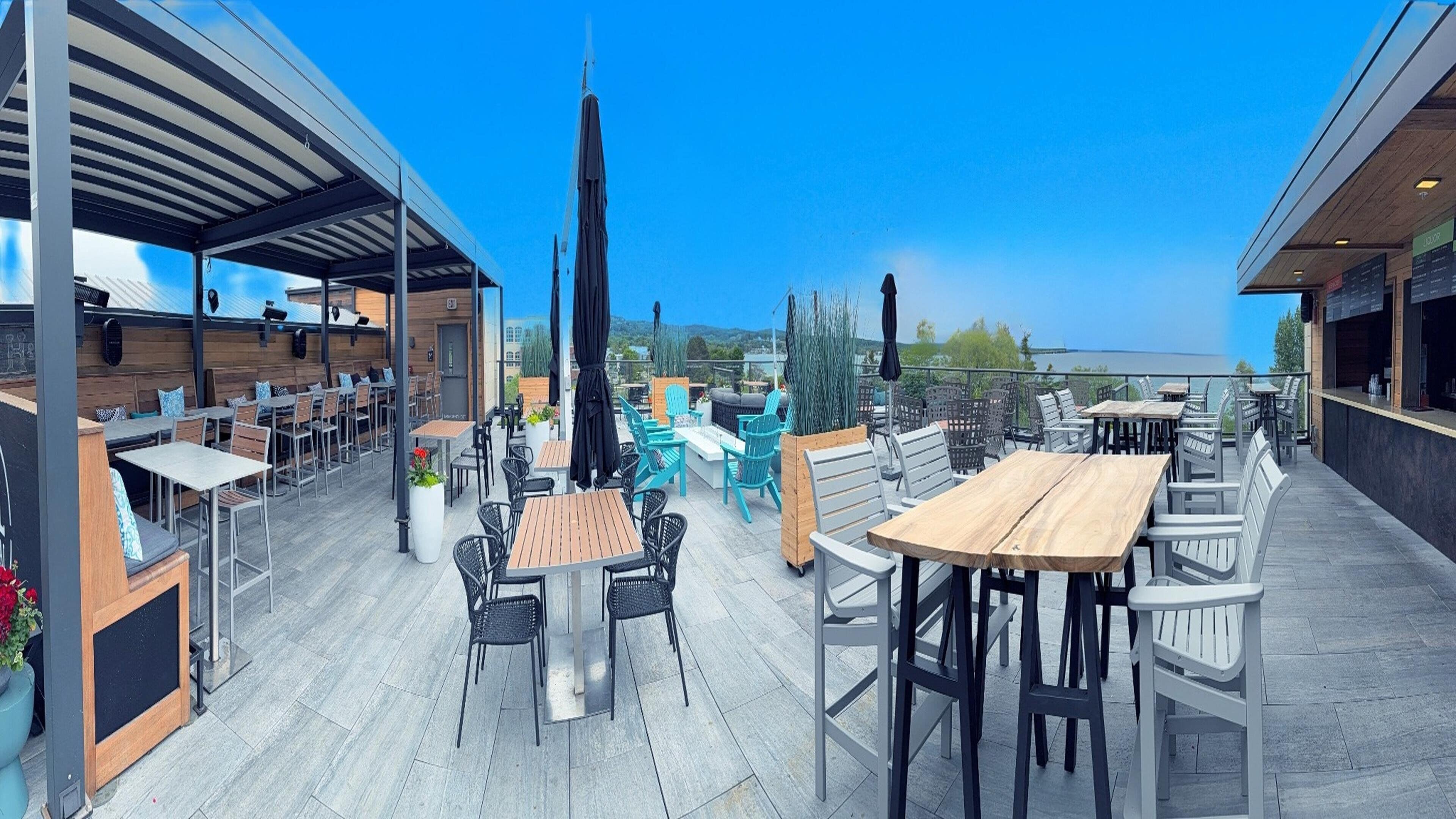 An outdoor patio with tables and chairs, a covered seating area, and a view of the water.