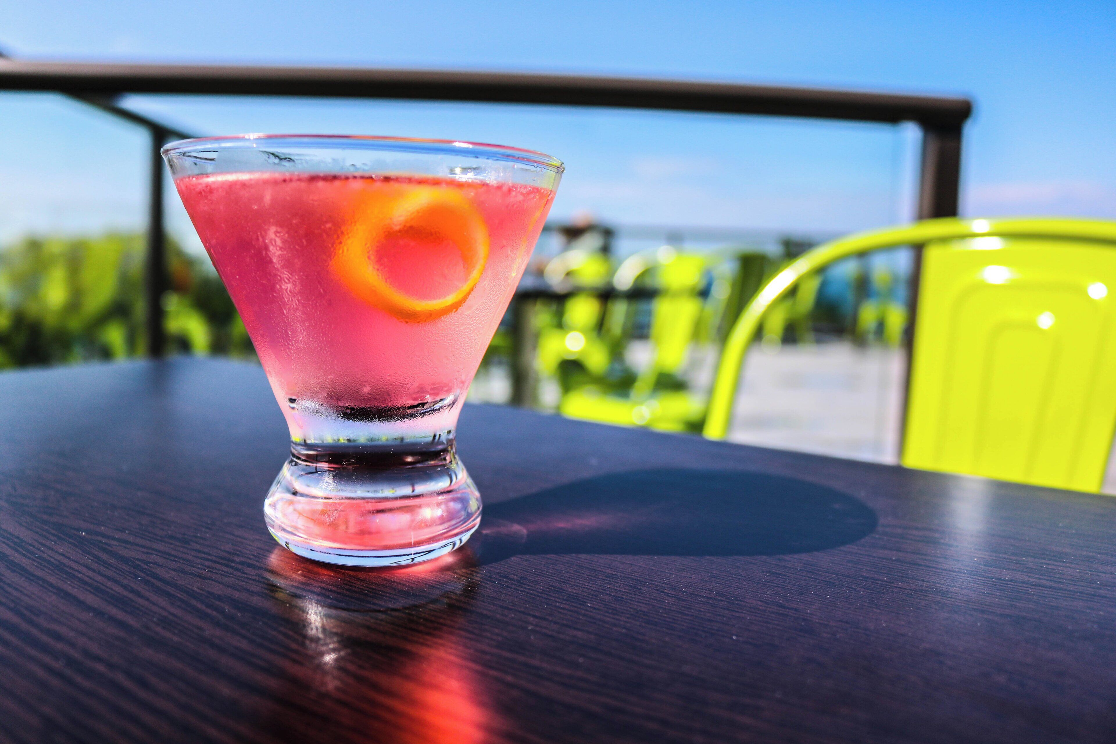 A cocktail glass with a slice of orange on a table outdoors.