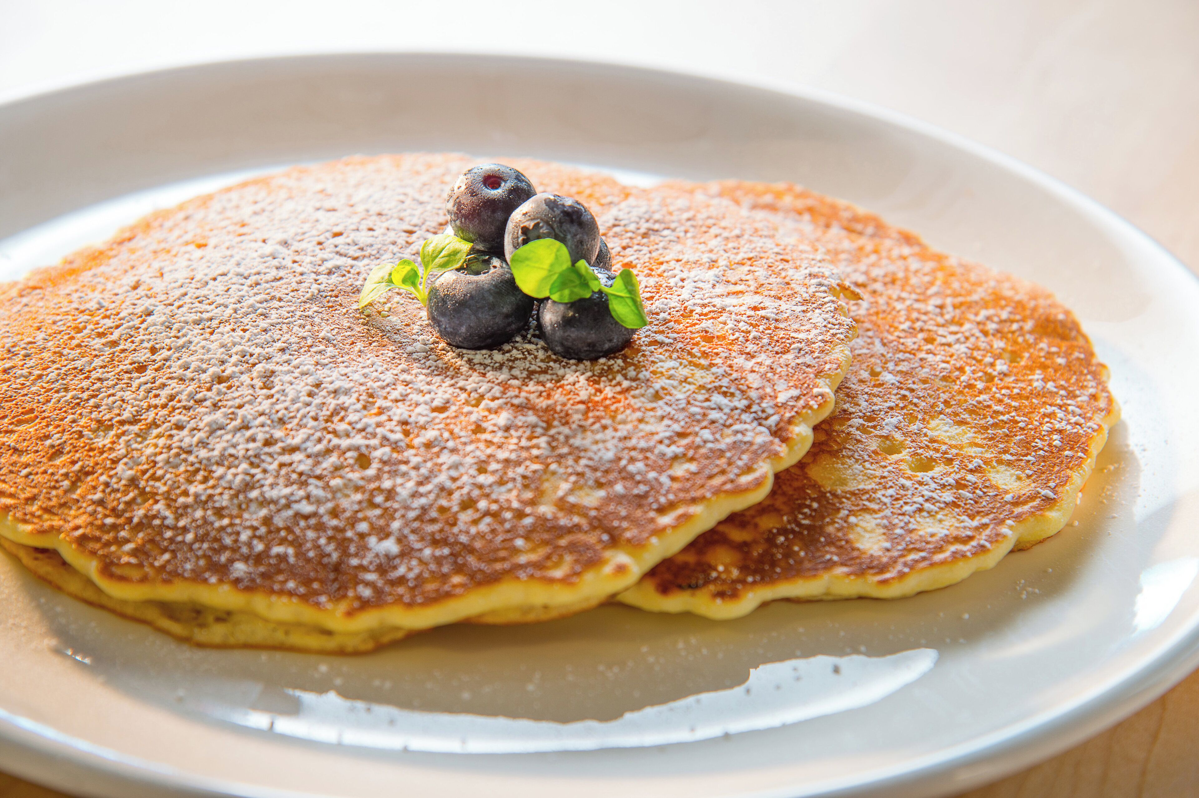 A plate with pancakes topped with blueberries and a dusting of powdered sugar.