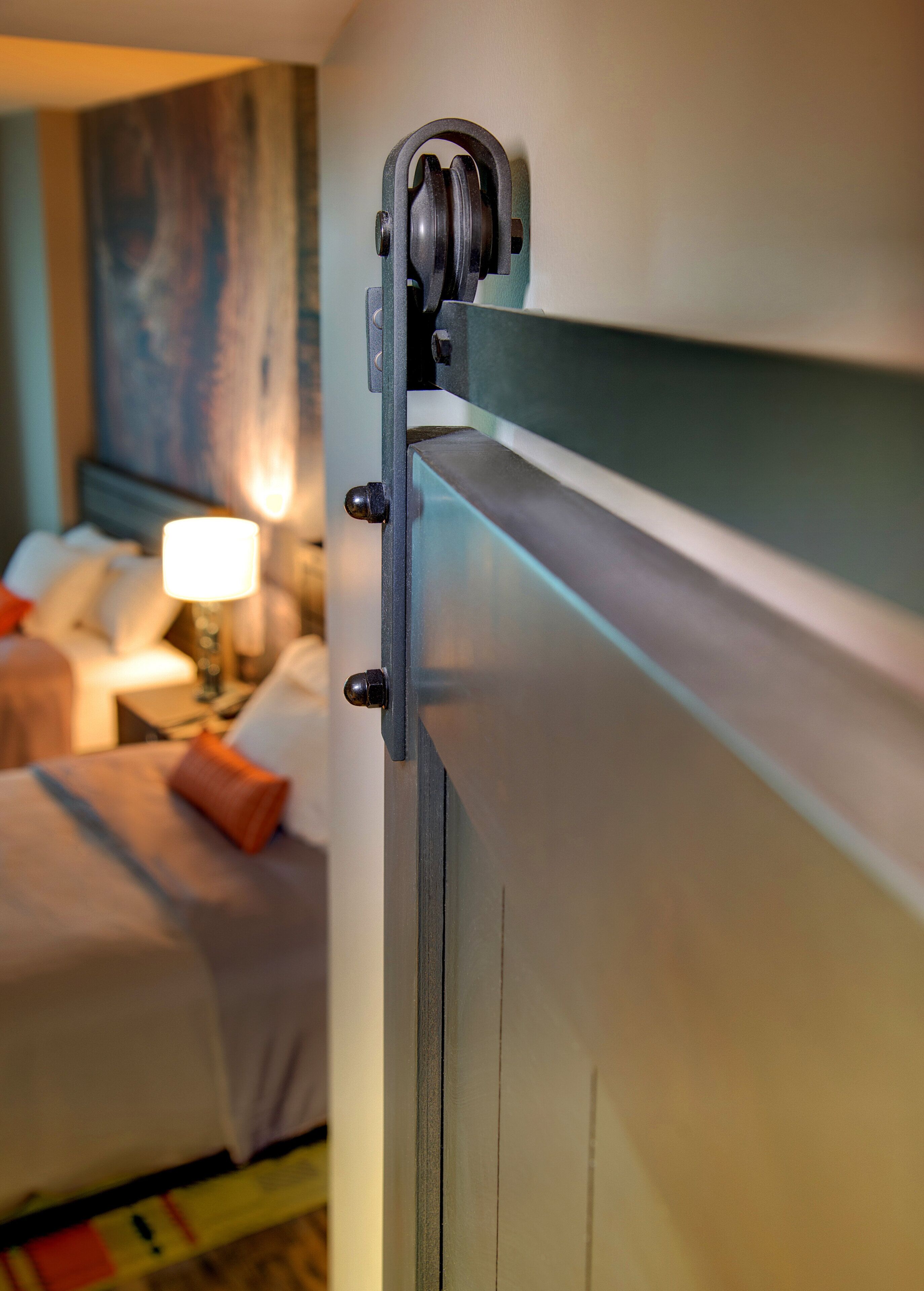 Quarto de hotel com cama, mesa de cabeceira, abajur e um quadro na parede.