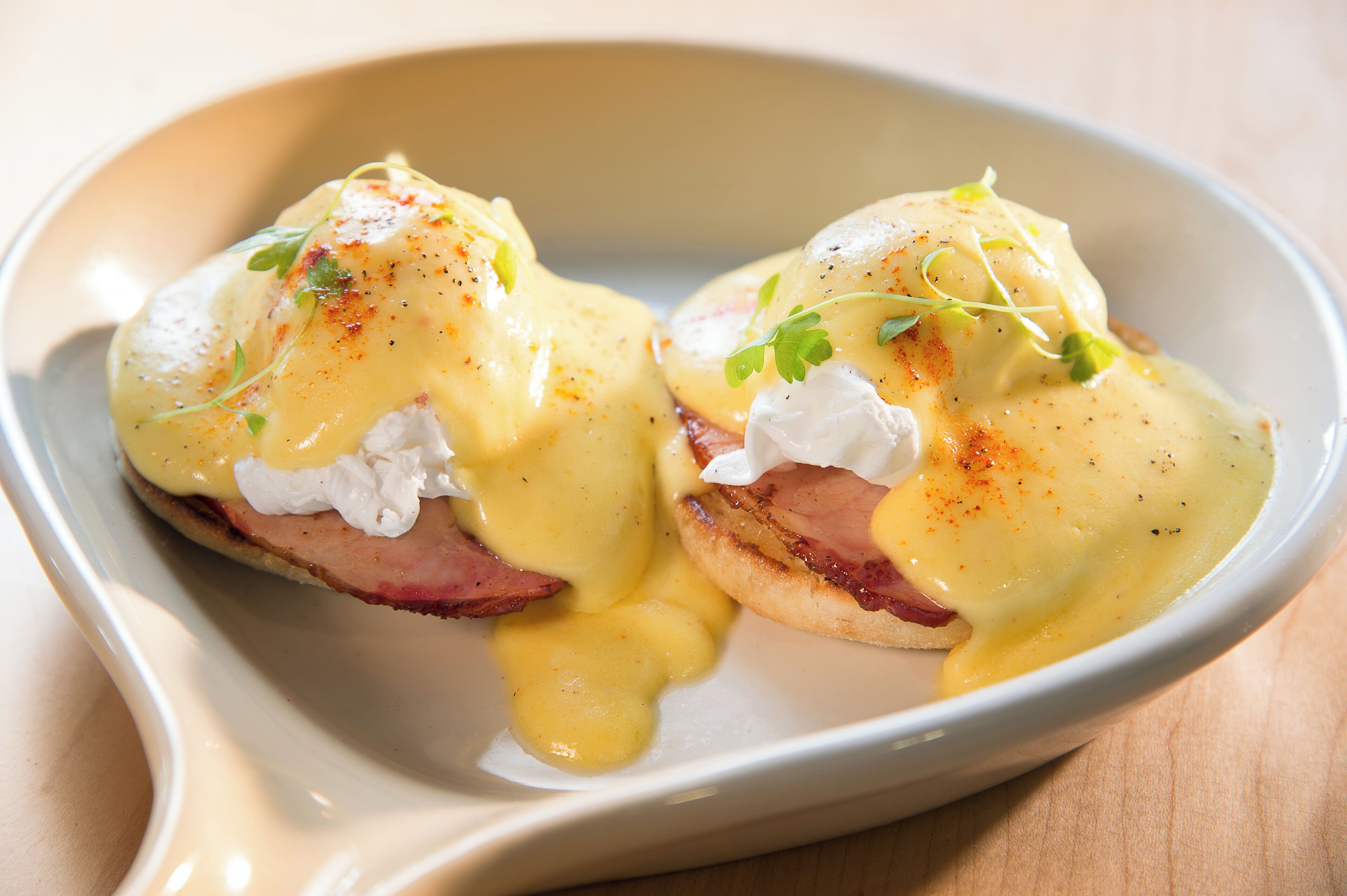 A dish of eggs benedict with hollandaise sauce, garnished with herbs.