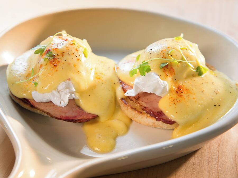 Un plato de huevos benedictinos con salsa holandesa, adornado con hierbas.