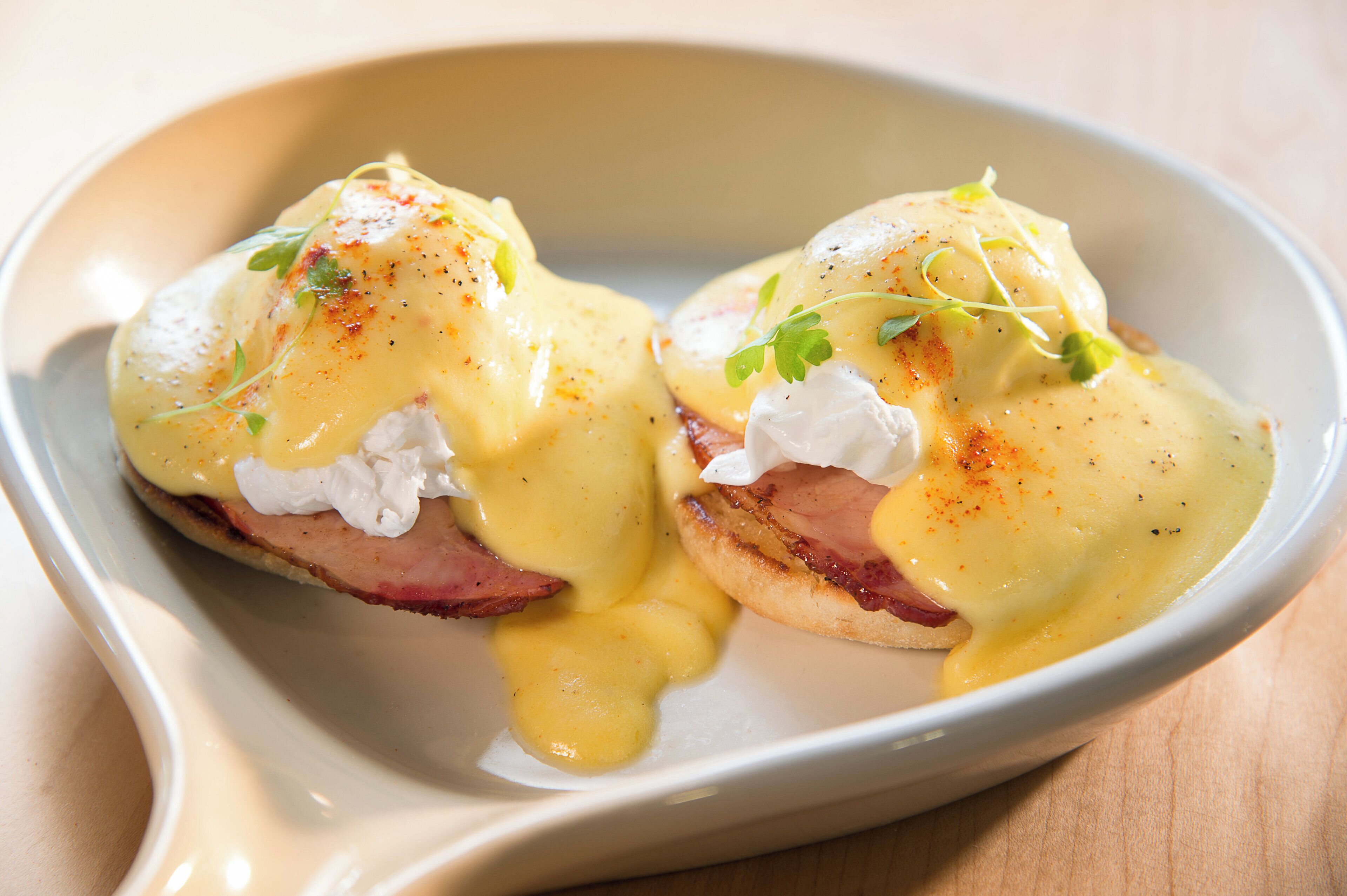 A dish of eggs benedict with hollandaise sauce, garnished with herbs.