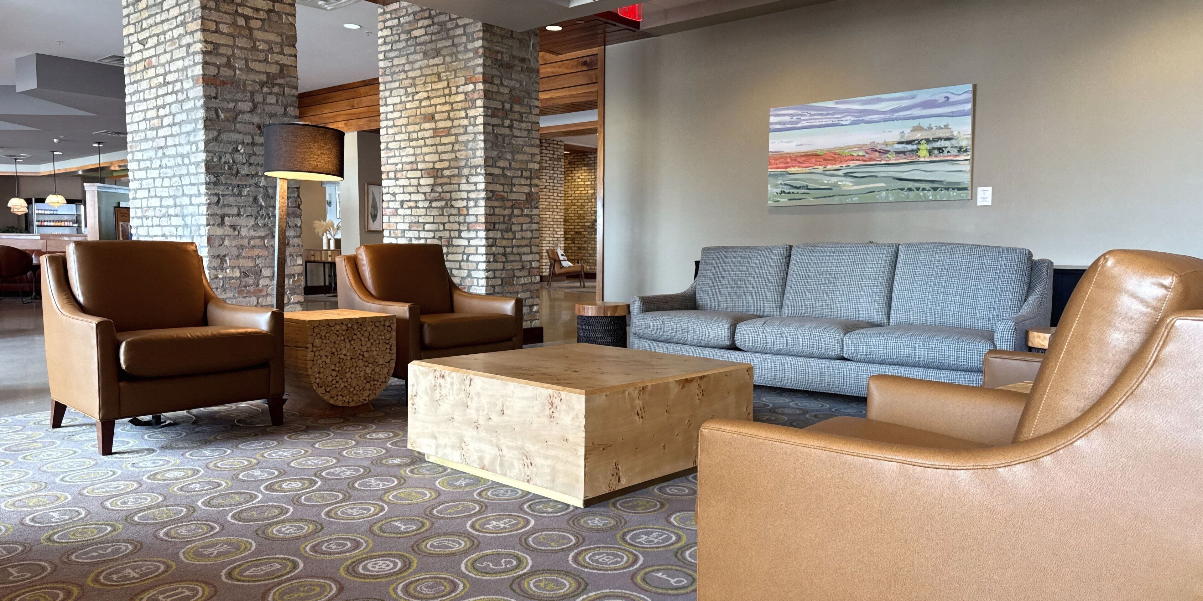 Eine Lobby mit Ledersesseln, einem Holztisch, einem gemusterten Teppich und einem Gemälde an der Wand.