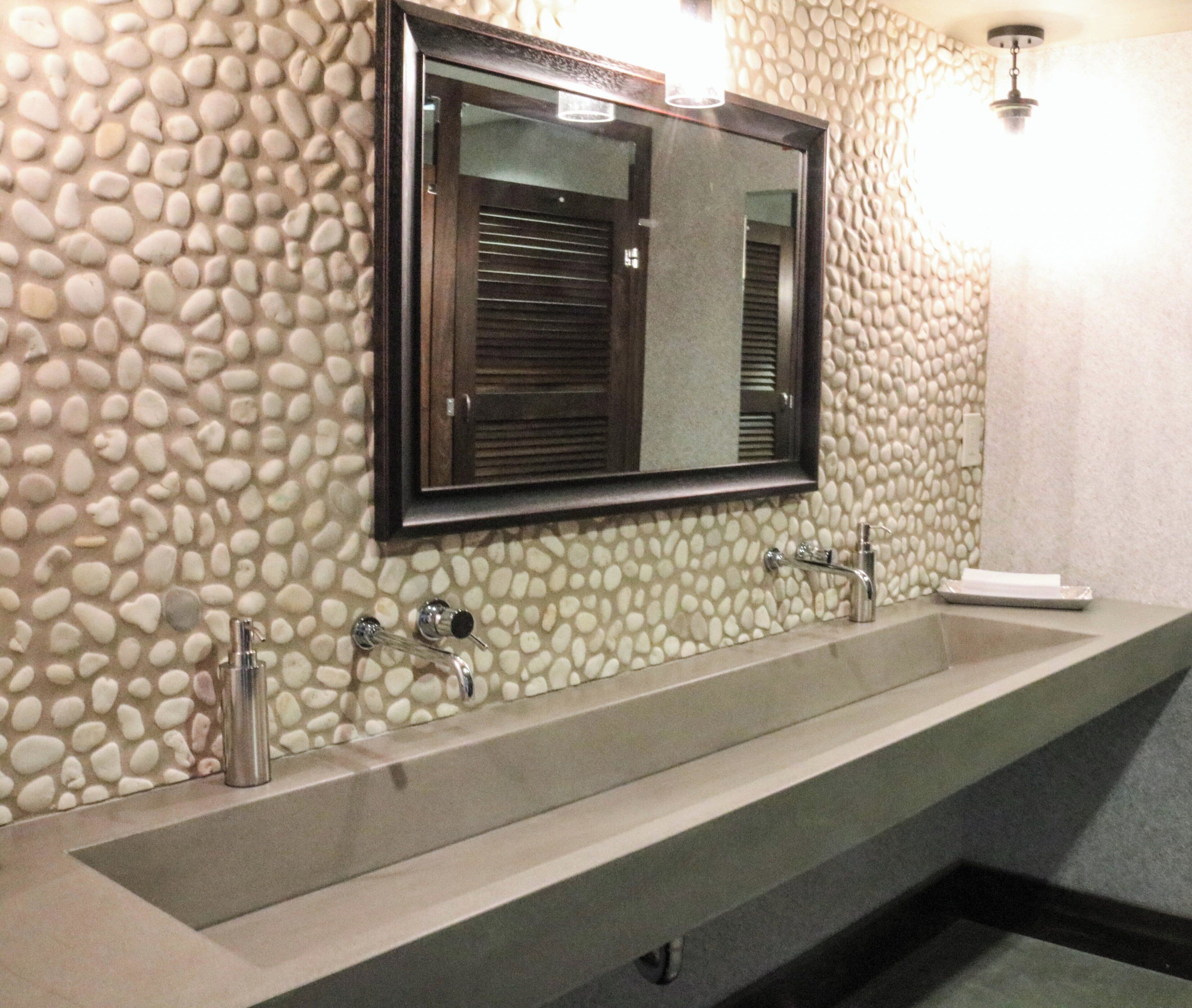 A bathroom with a pebble-patterned wall, a large mirror, and a dual sink with faucets.
