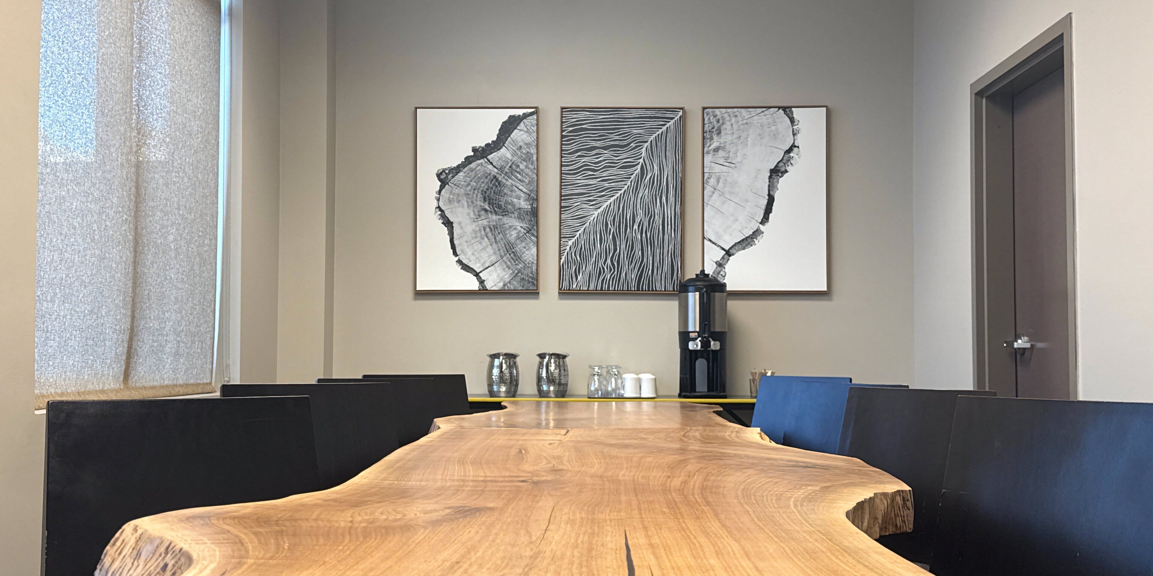 Una sala conferenze con un lungo tavolo di legno, sedie imbottite nere e tre opere d'arte appese al muro.