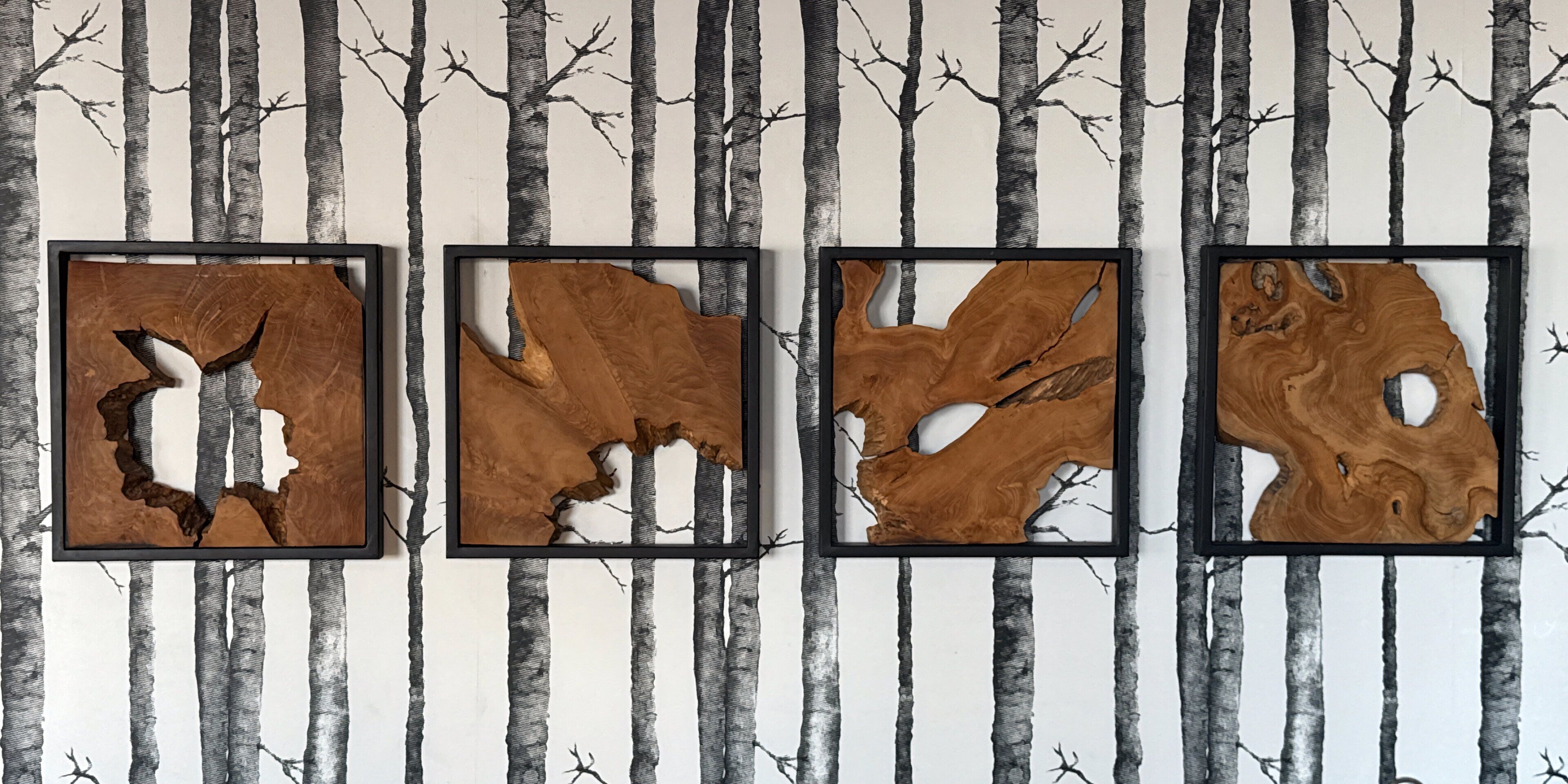 Cuatro cuadros de madera en una pared, con un fondo de diseño de abedul.