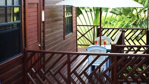 Una terraza de madera con una sombrilla blanca, una silla y una mesita.