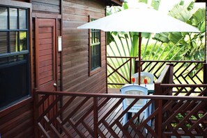 A wooden deck with a white umbrella, a chair, and a small table. - Yellow Bird Apartment (Silver Sands)