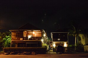 A two-story wooden house with a balcony, a car parked in front, and a palm tree nearby. - Yellow Bird Apartment (Silver Sands)