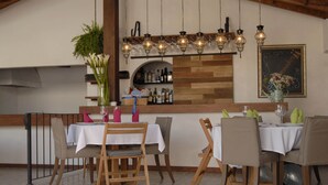 Un comedor con mesas y sillas de madera, una barra con botellas, y lámparas colgantes.