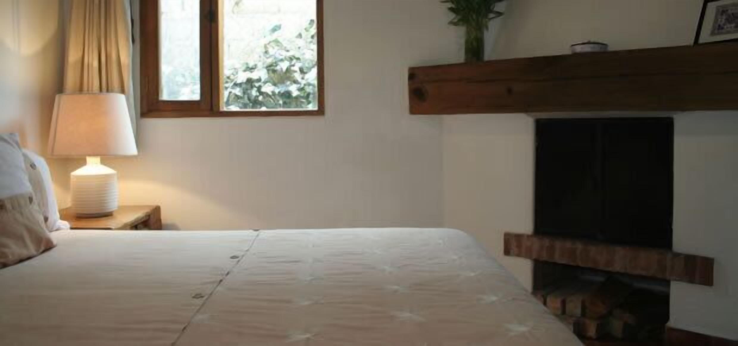 A bedroom with a bed, a bedside lamp, a window with curtains, and a fireplace.