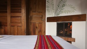 Una habitación con una cama, una puerta de madera, una chimenea encendida y una pared con un diseño de hojas.