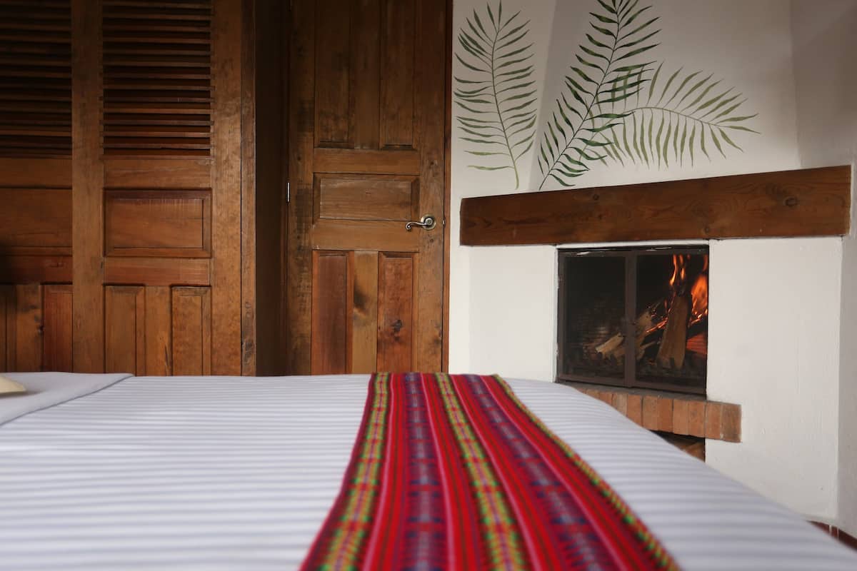 A room with a bed, a wooden door, a fireplace with a fire, and a wall with a leaf design.